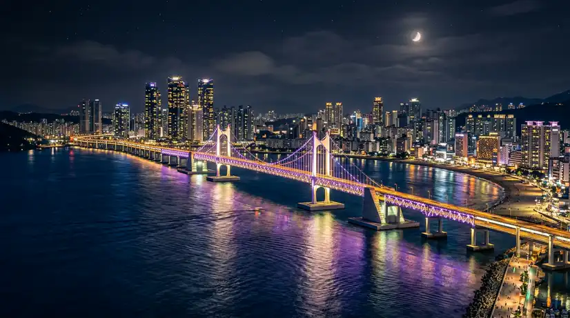 Illuminated Gwangandaegyo Bridge with purple and gold LED lights spanning ocean with glowing city skyline reflection
