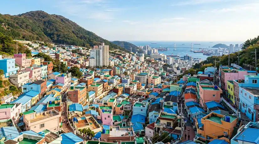 Wide-angle view of hillside Gamcheon Village with pastel blue, pink, and yellow houses under morning light and ocean