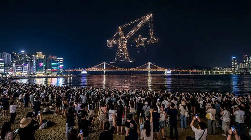 Hundreds of illuminated drones forming glowing pattern above Gwangan Bridge with crowds watching in awe 