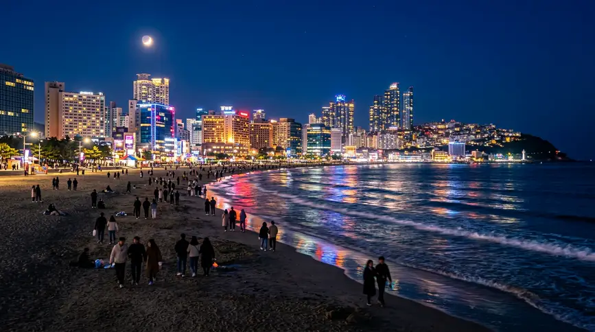 Shoreline illuminated by city lights and moon with neon reflections shimmering on gentle waves
