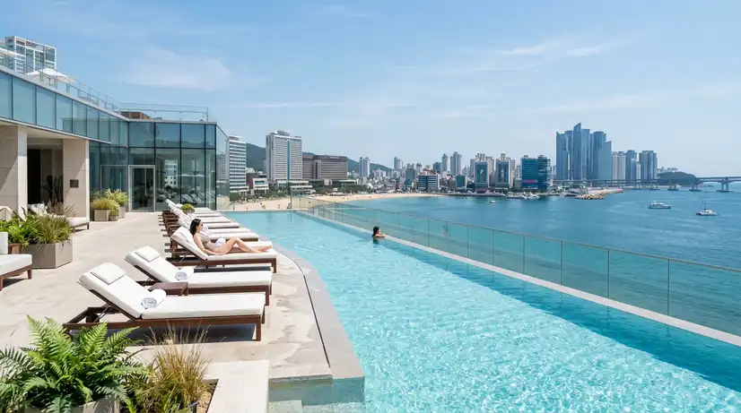 Crystal clear infinity pool at high-end Busan spa with modern loungers and glass railings above ocean coastline