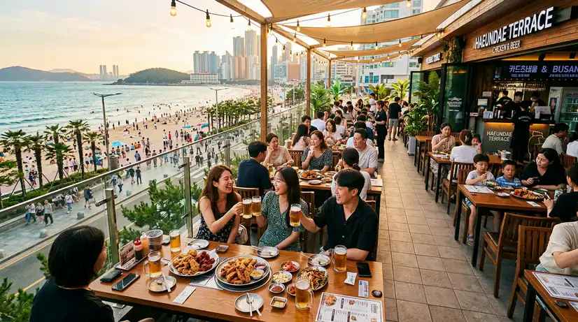 Wide view of beachfront terrace with groups enjoying fried chicken and beer during golden hour at Haeundae

